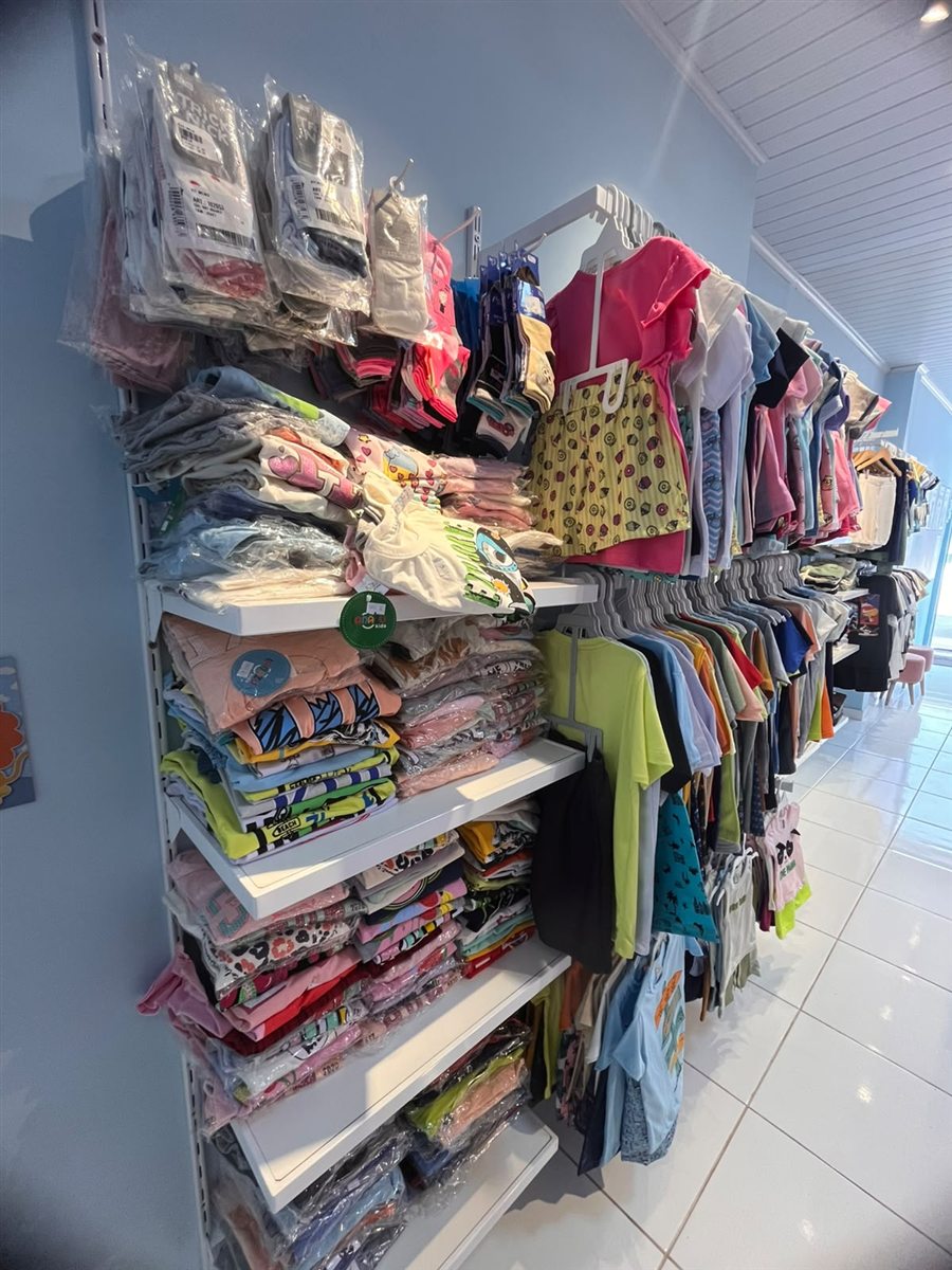 Parede azul-clara da DM Kids com prateleiras e araras de roupas infantis