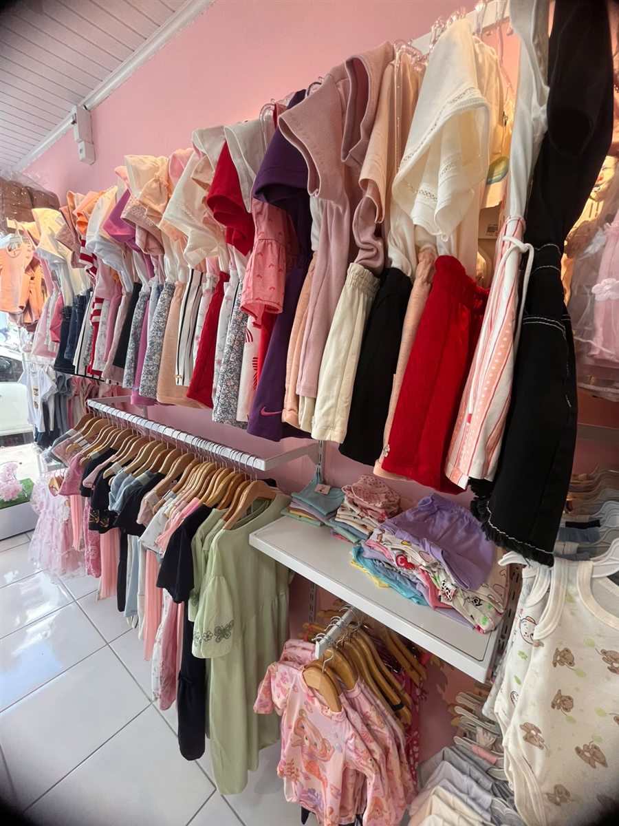 Parede rosa da DM Kids com araras de roupas infantis coloridas